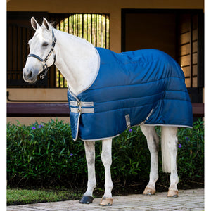 HORSEWARE Amigo Insulator 50gr in Blau auf weißem Pferd vor Stallkulisse. Leichte Pferdedecke aus der Standardkollektion, frisch eingetroffen.