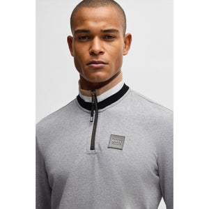 Detailansicht des grauen BOSS Herren Troyer Sweaters mit Logo-Patch und Reißverschlusskragen, gefertigt aus elastischem Sweat-Material.