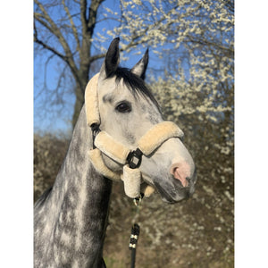 Graues Pferd mit One Equestrian Lammfellhalfter aus synthetischem Schaffell vor blühenden Bäumen. Komfortables Halfter für Pferde in Beige-Schwarz.