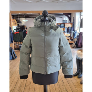 LeMieux Kinder Winterjacke Daisy in Salbeigrün mit abnehmbarer Kapuze und Sturmbündchen, präsentiert auf einer Schneiderpuppe in einem Reitsportgeschäft.