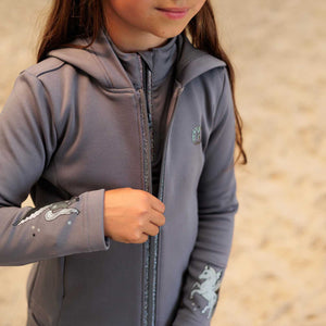 Mädchen trägt IRHIzzy Kinder Kapuzenjacke mit Reißverschluss und Pferde-Prints, ideal für stylische Winterabenteuer in der Reitmode.
