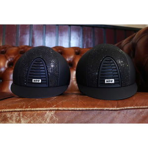 Kep Cromo 2.0 Reithelm - Textil Glitter in Schwarz mit Glitzereinsatz auf braunem Ledersofa, ideal für stilbewusste Reiterinnen.