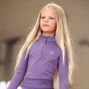 Mädchen trägt das Imperial Riding Kinder Langarmshirt IRHAbby mit Glitzerdetails und Kinnschutz – perfekt für stilvolle Winteroutfits.