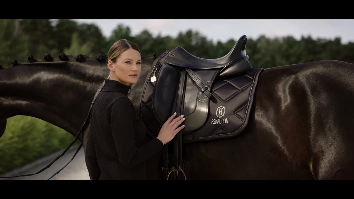 Eskadron brand image: woman beside a bay horse with a black Eskadron saddle pad outdoors.