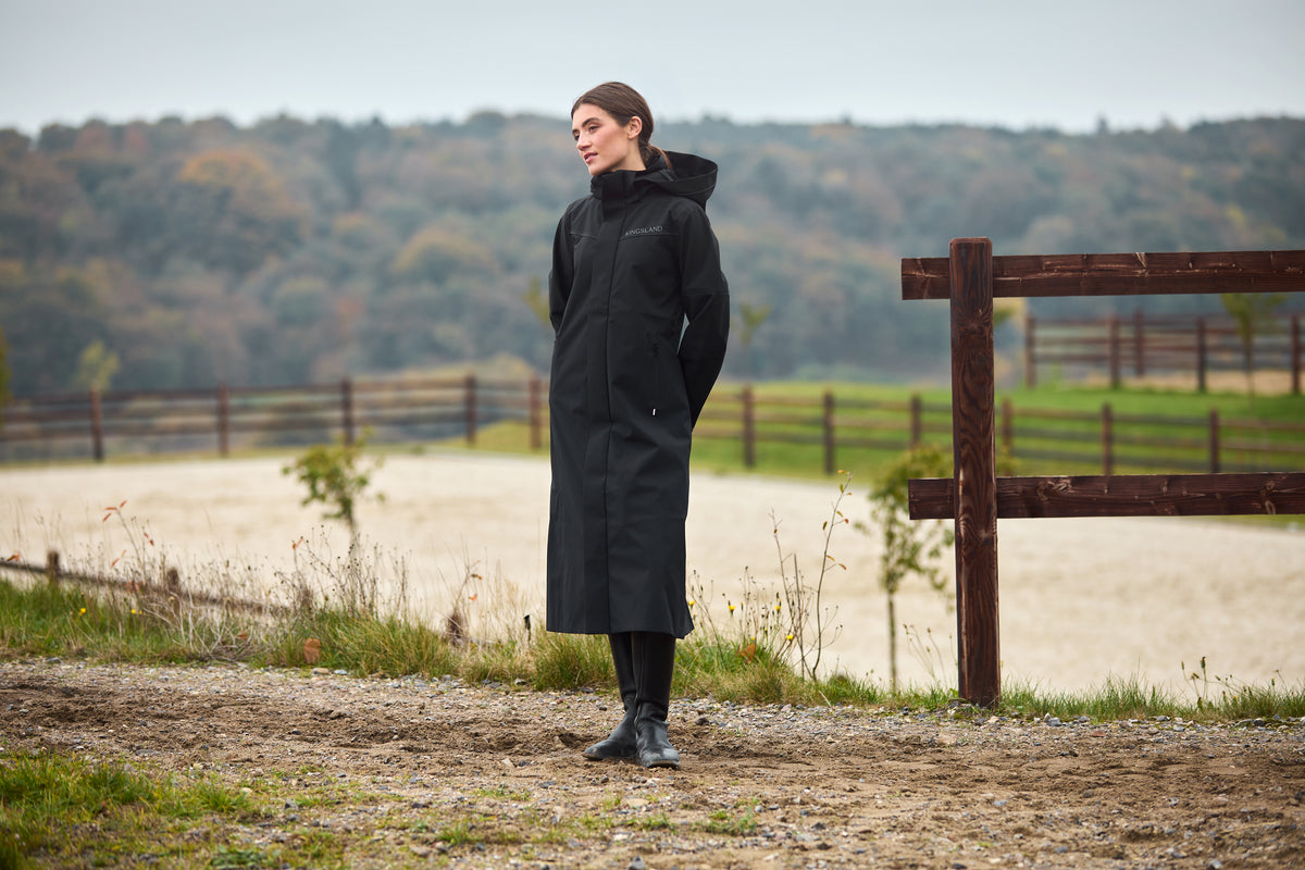 Kingsland brand image: woman in a black riding coat beside a paddock in autumn.